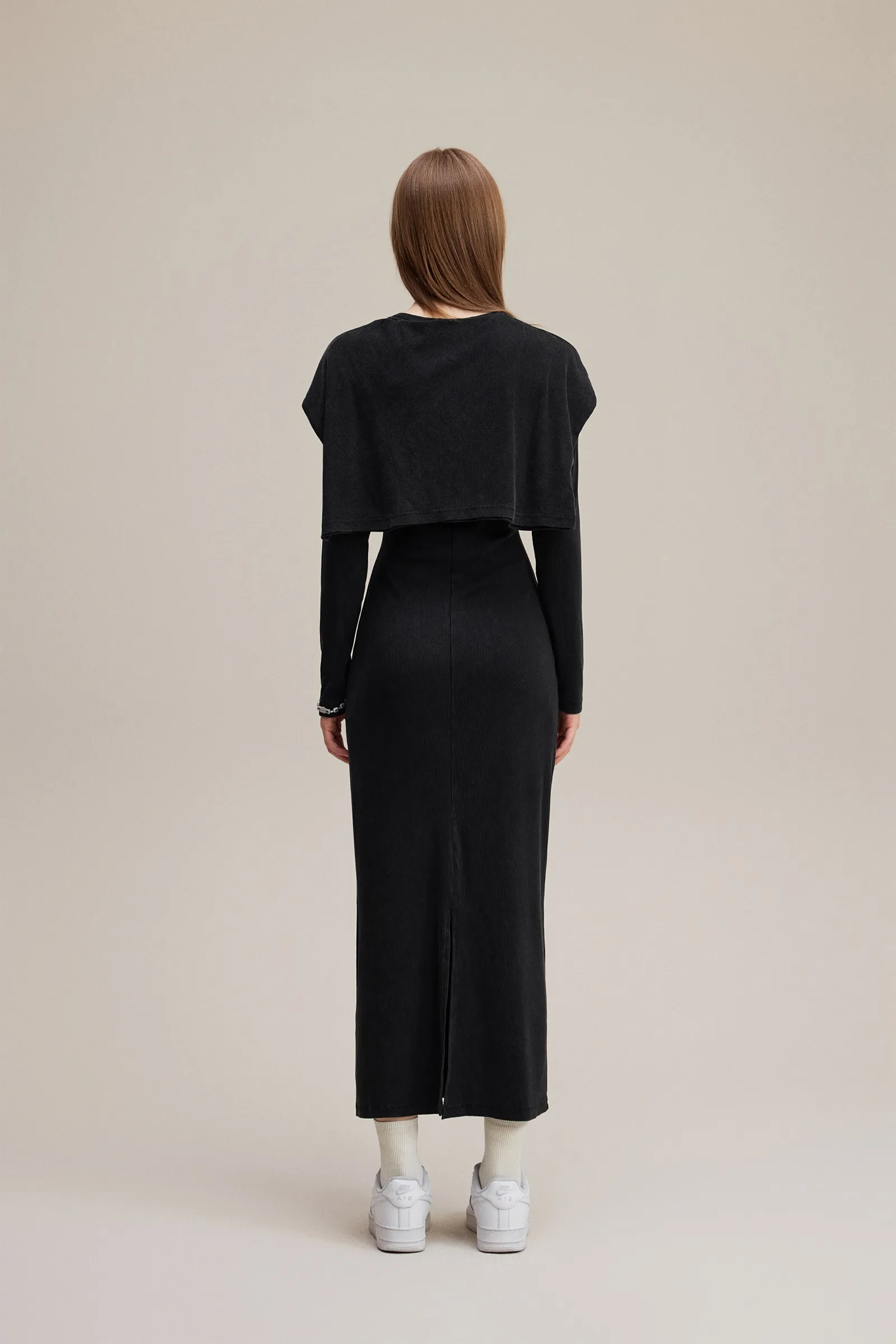 Person wearing a black outfit with a cropped top and long skirt on a beige background