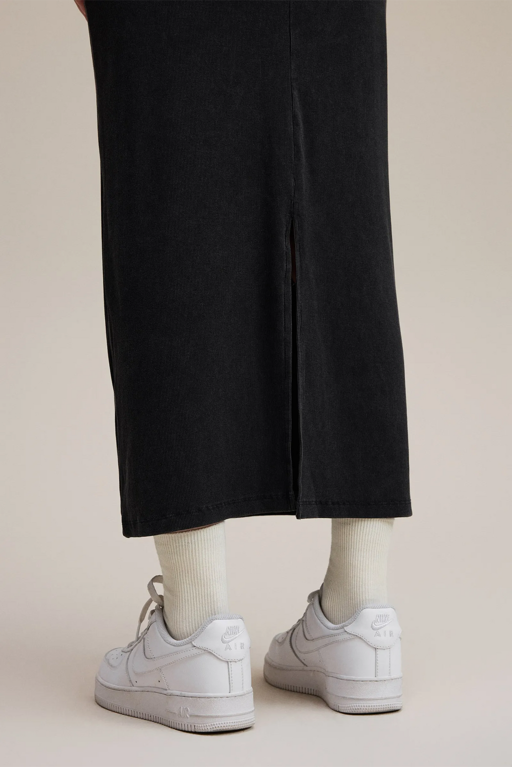 Person wearing black pants and white sneakers on a beige background