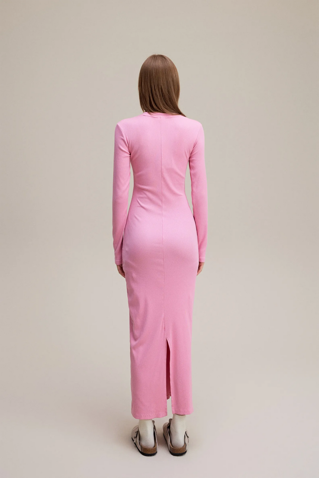 Person wearing a pink dress with a back slit on a beige background