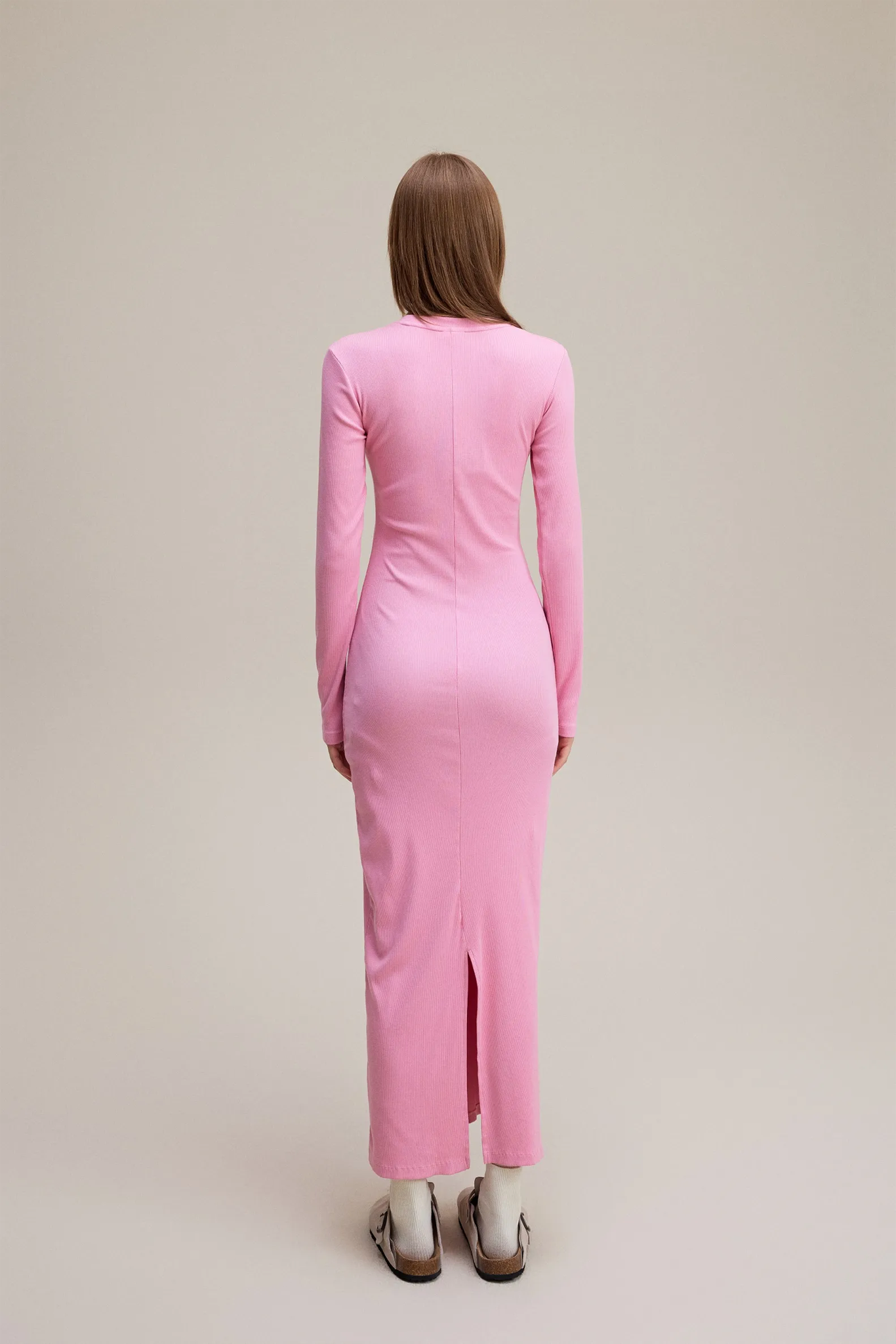Person wearing a pink dress with a back slit on a beige background