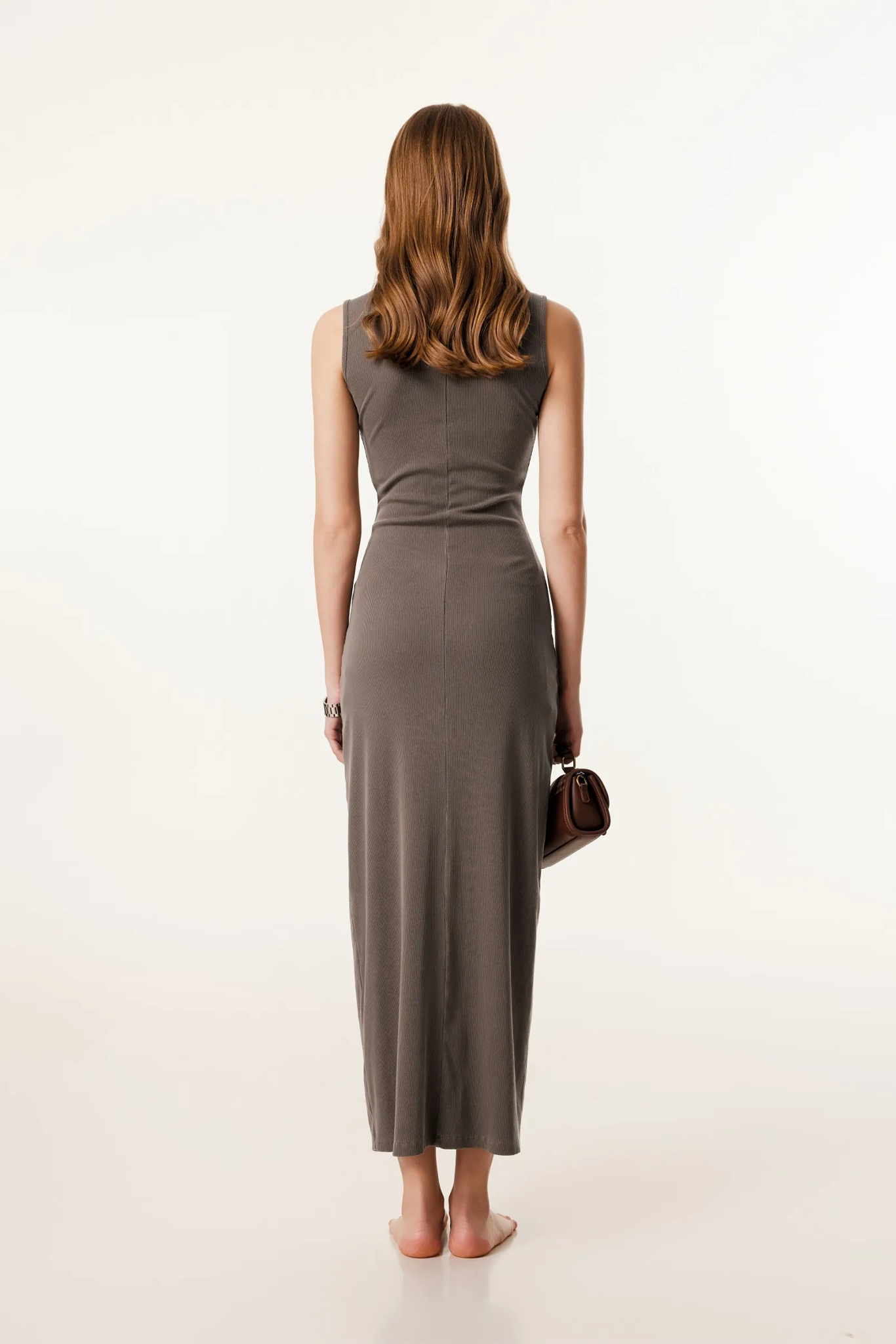 Woman wearing a long brown dress holding a handbag on a white background