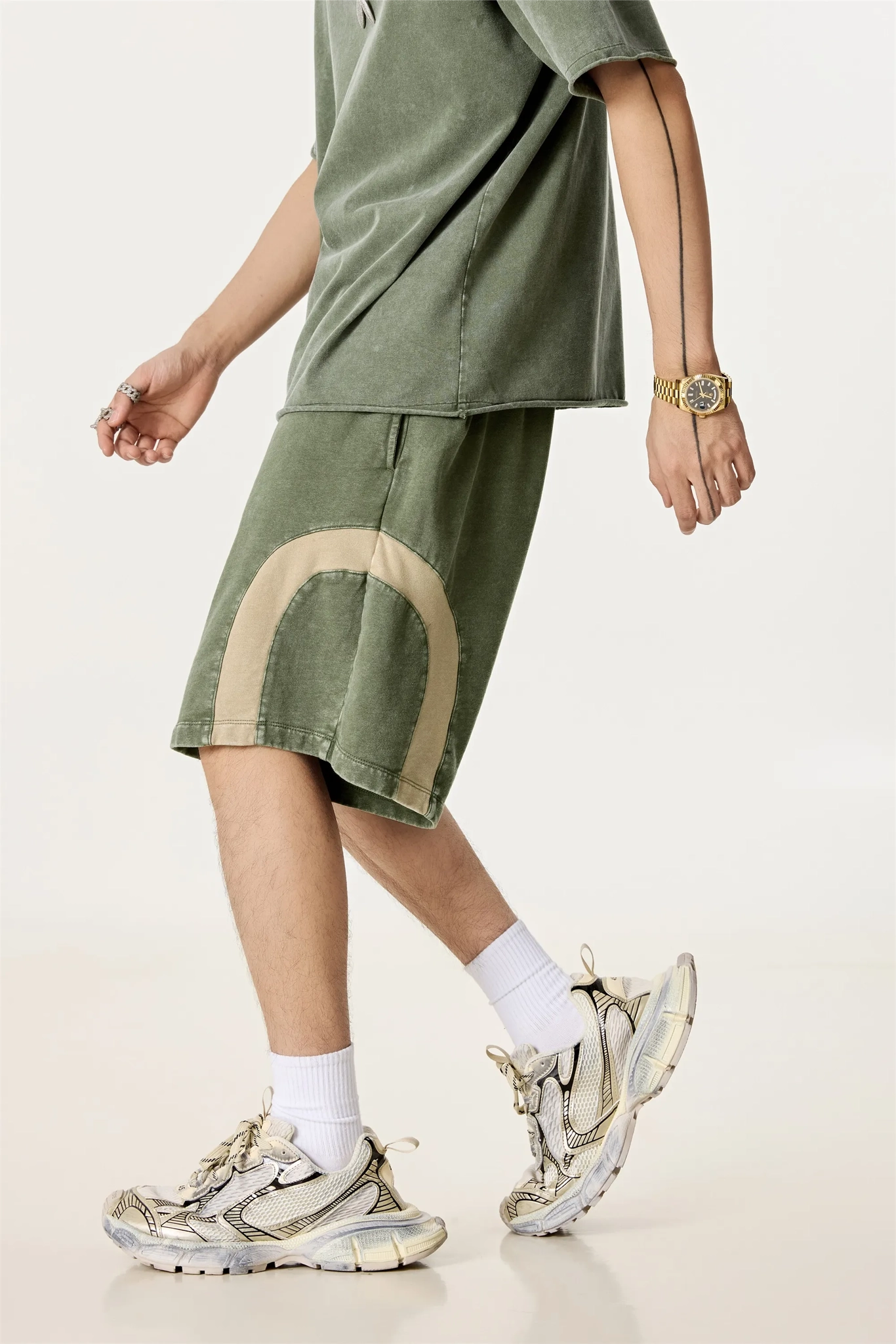 Person wearing green oversized shirt and shorts with white sneakers on a light background