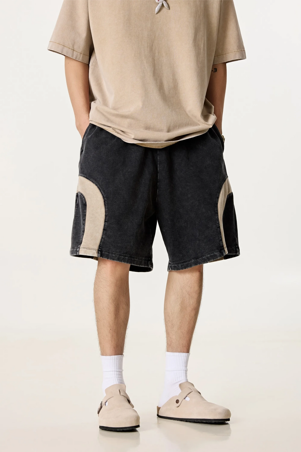 Person wearing a beige t-shirt and black shorts with white accents on a plain background