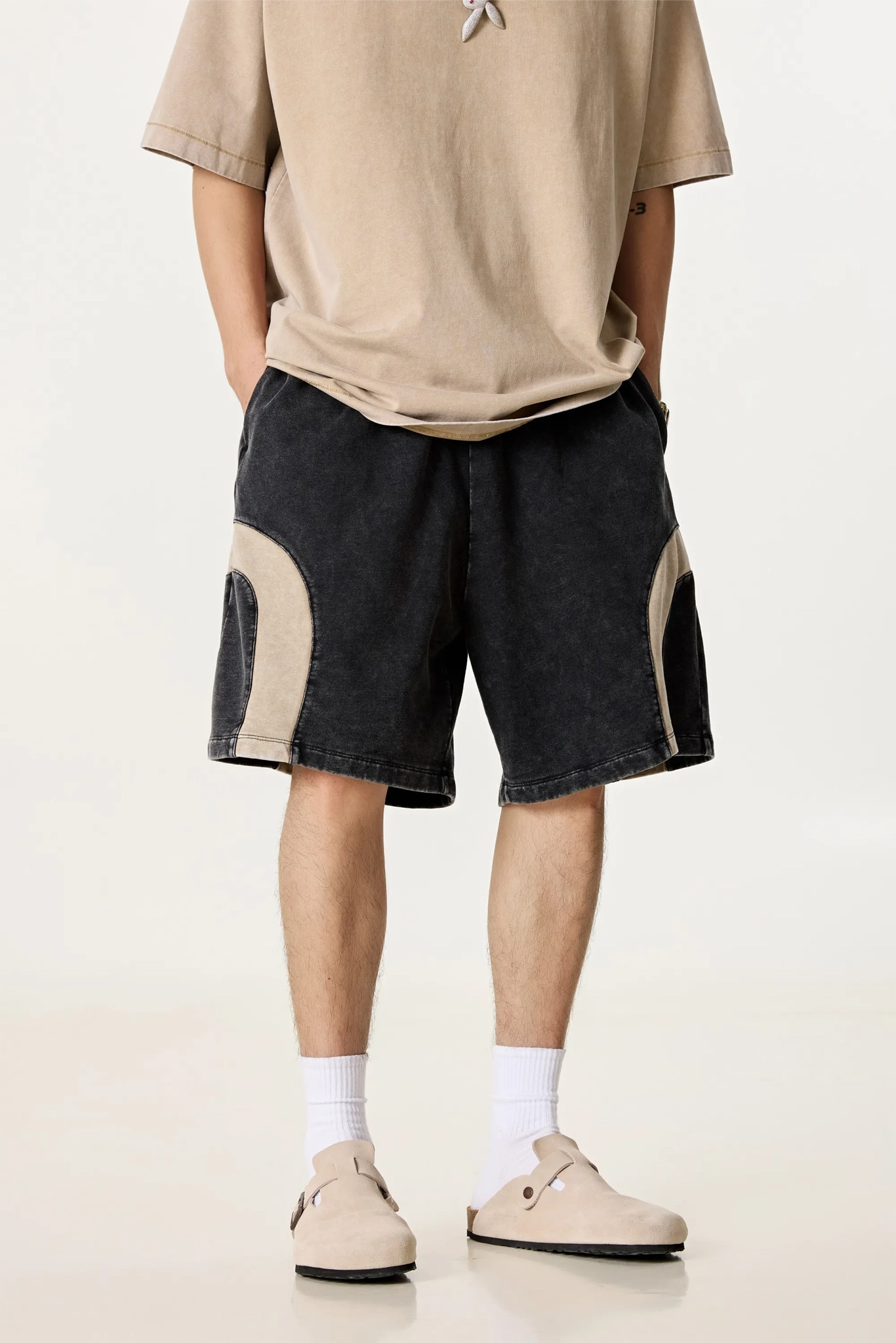 Person wearing a beige t-shirt and black shorts with white accents on a plain background