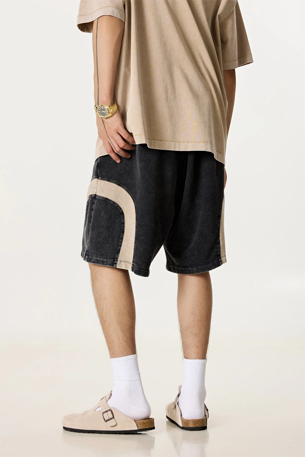 Person wearing a beige t-shirt, black shorts with beige accents, white socks, and beige shoes on a light background