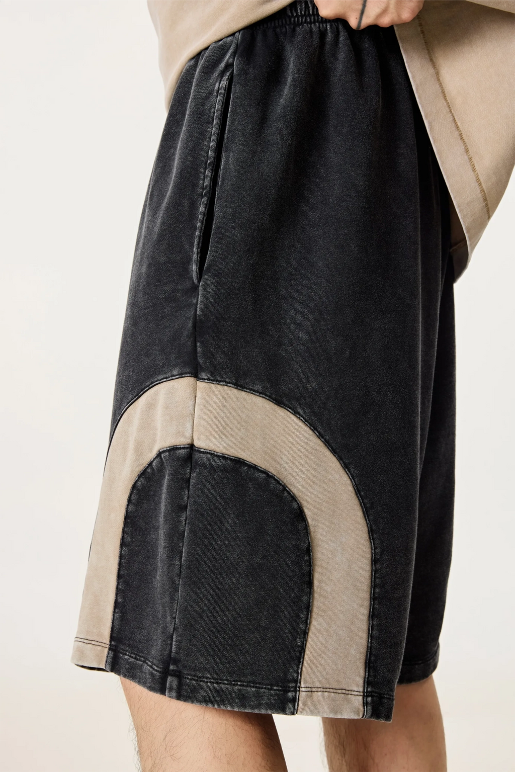 Black and beige shorts worn by a person on a plain background