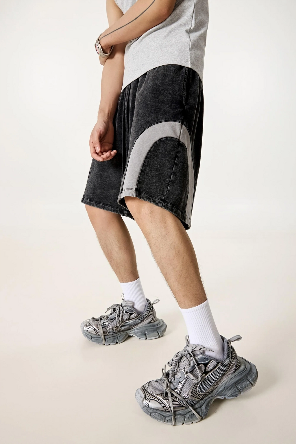 Person wearing black shorts with a sheer panel, white socks, and gray sneakers on a plain background