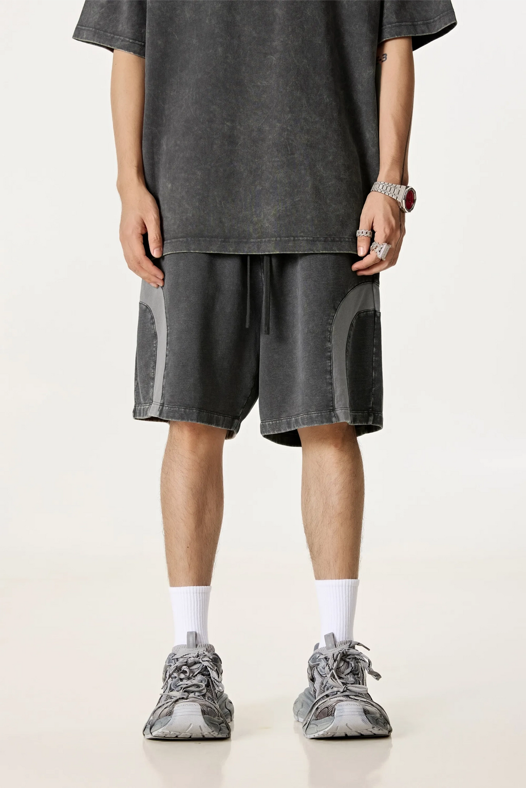 Person wearing a gray oversized t-shirt and shorts with white socks and gray sneakers on a light background