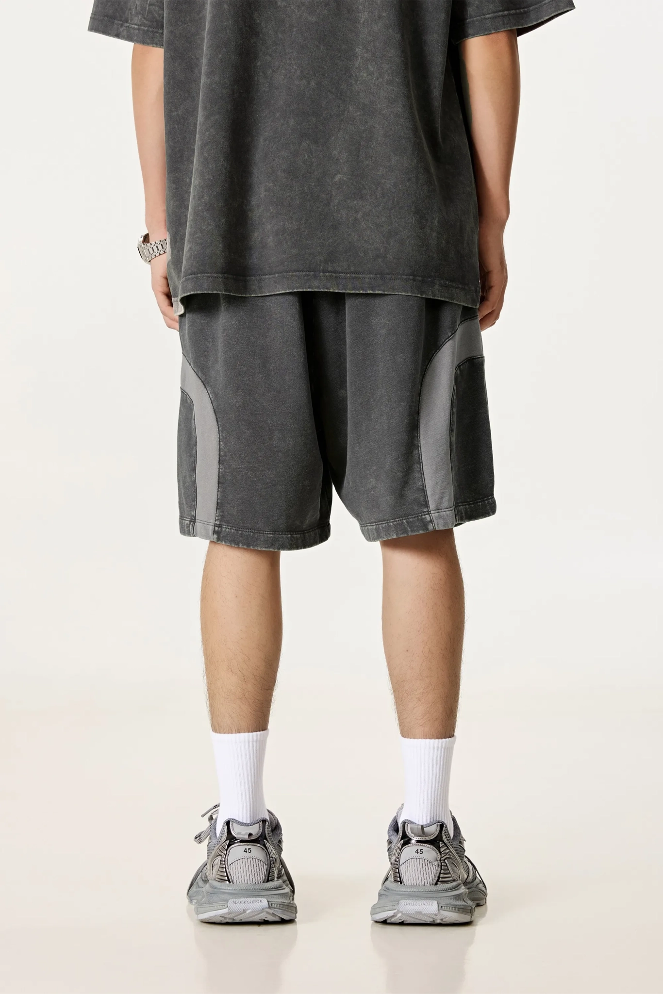 Person wearing a dark gray t-shirt and shorts with white socks and sneakers on a light background