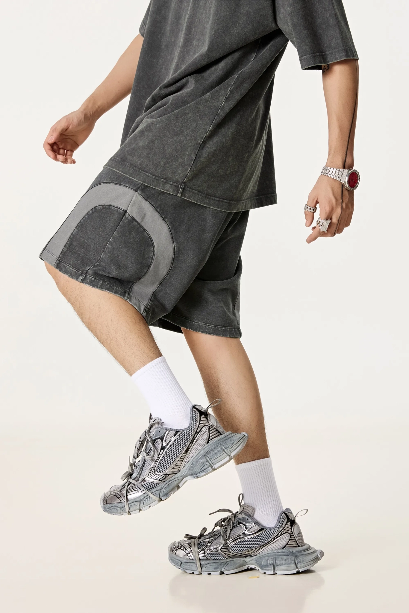 Person wearing a dark gray oversized t-shirt and shorts with white socks and gray sneakers on a light background