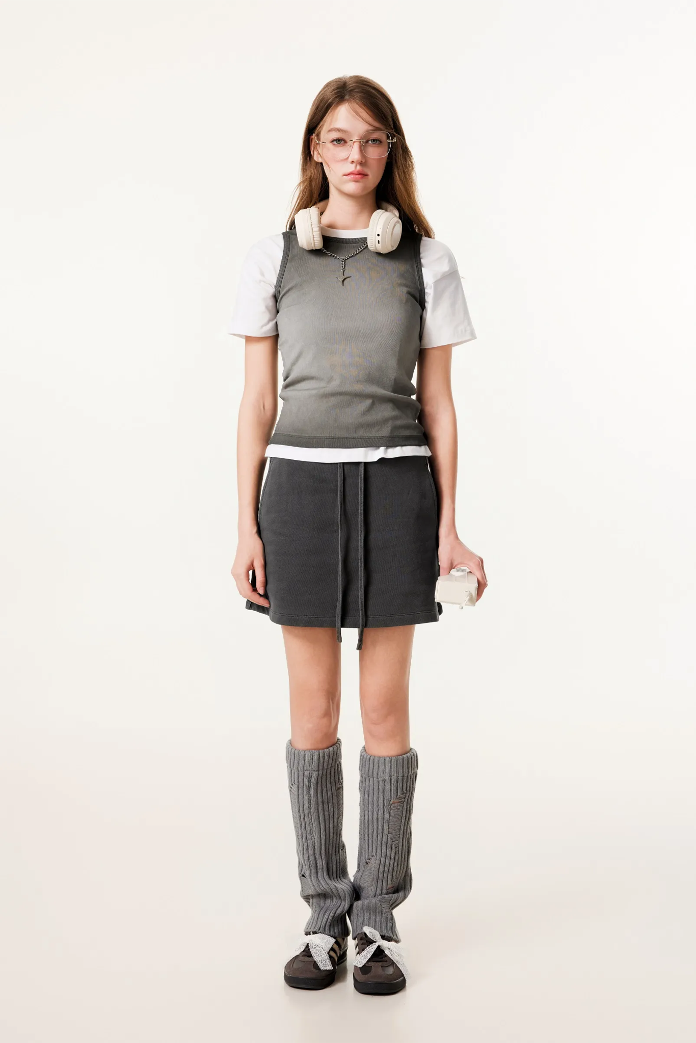 Woman wearing a gray outfit with a white shirt, skirt, and knee-high socks on a white background