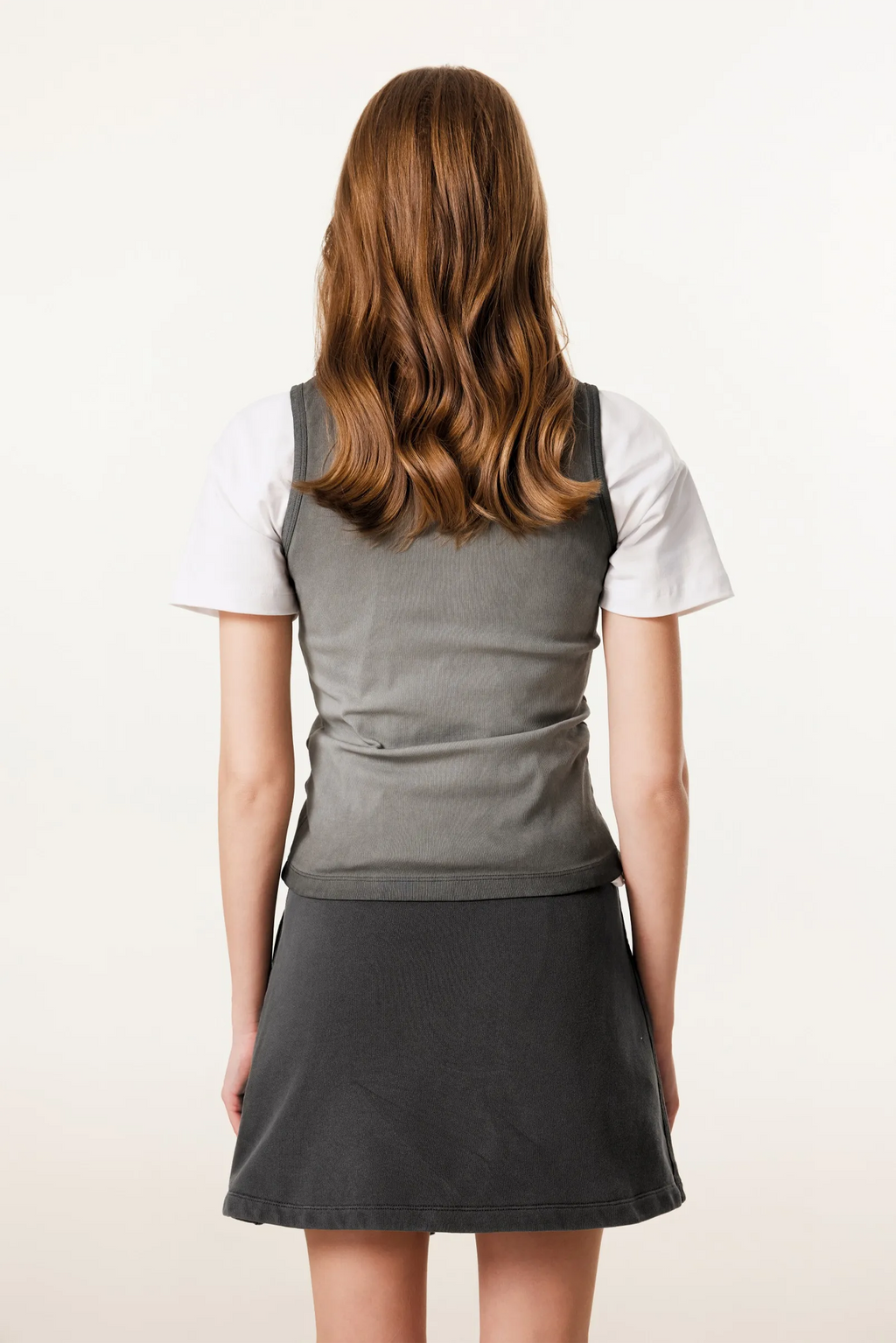 Person wearing a gray dress with a white shirt underneath on a plain background