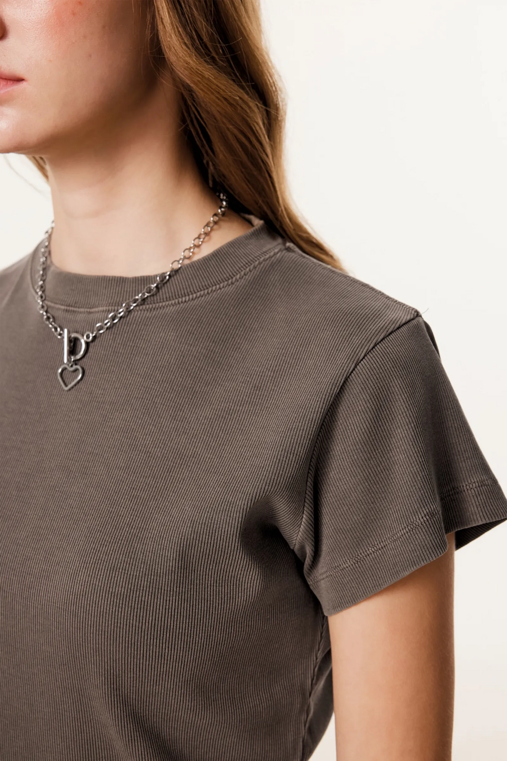 Person wearing a brown t-shirt and a necklace with a heart pendant on a plain background