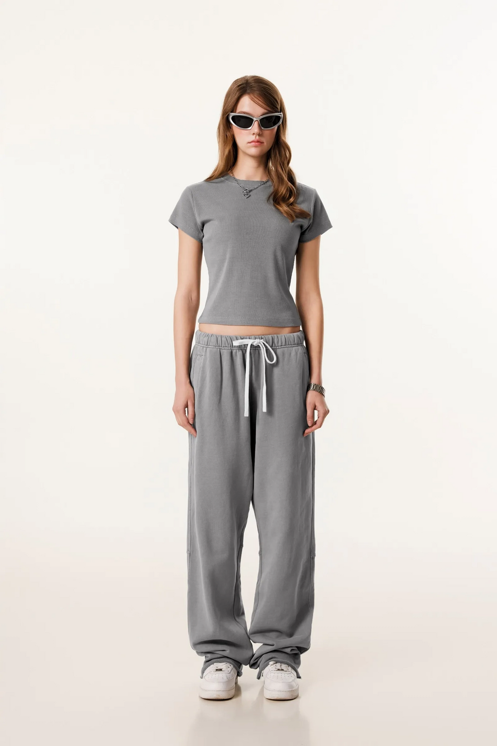 Woman wearing a gray t-shirt and pants with sunglasses on a white background