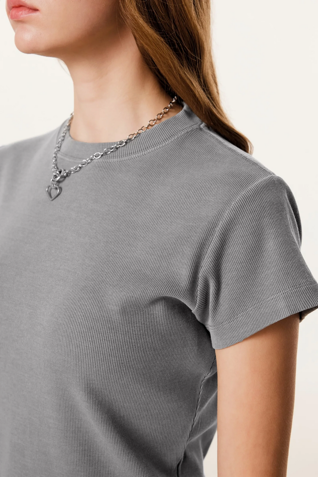 Person wearing a gray t-shirt and a chain necklace on a plain background