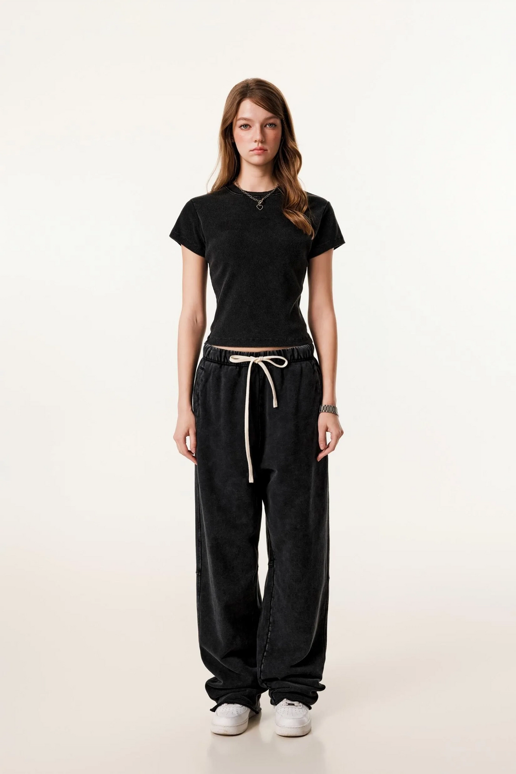 Person wearing a black t-shirt and black pants with a white drawstring on a beige background