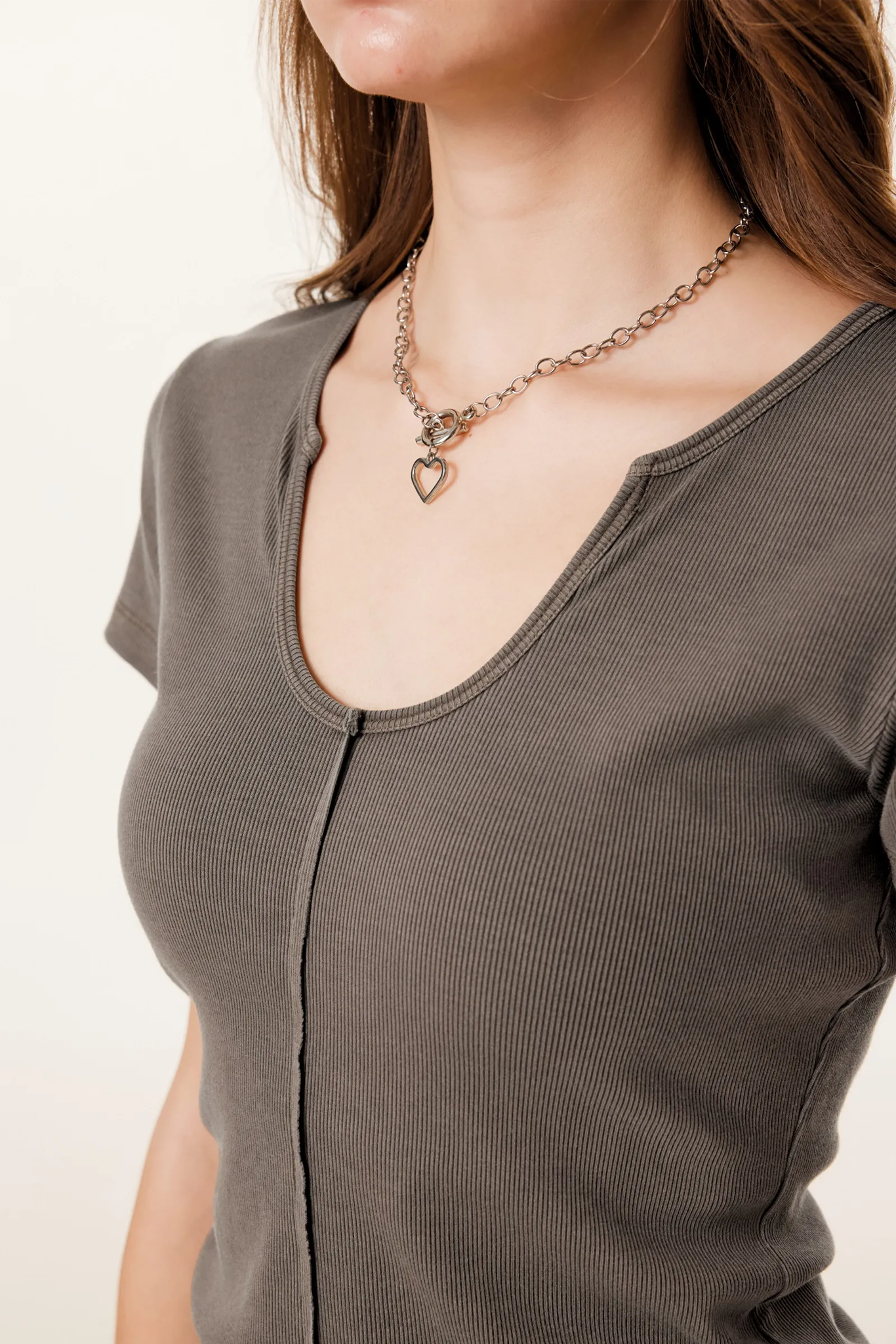 Woman wearing a brown top and a necklace with a heart pendant on a plain background