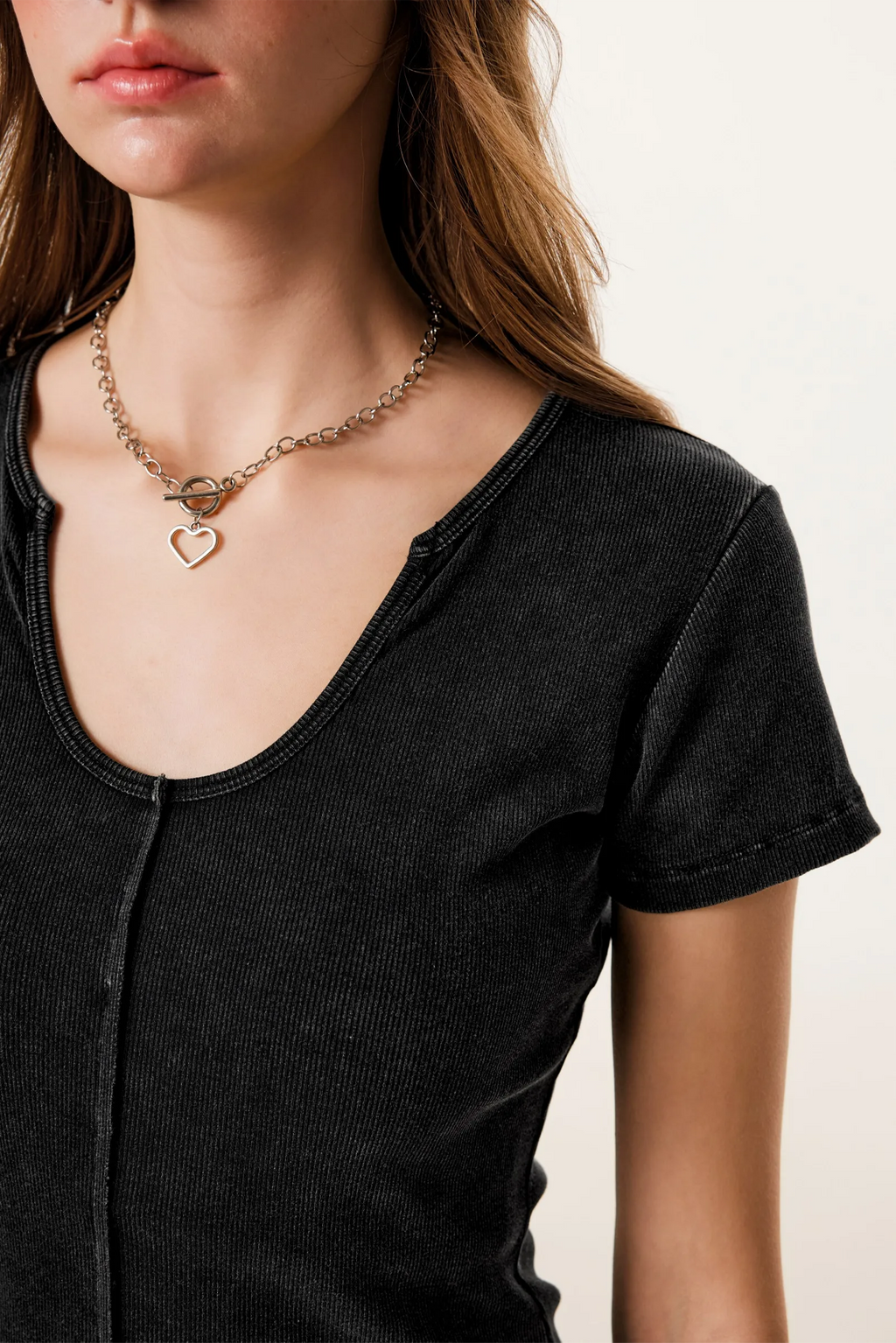 Person wearing a black shirt and gold necklace with heart pendants on a neutral background