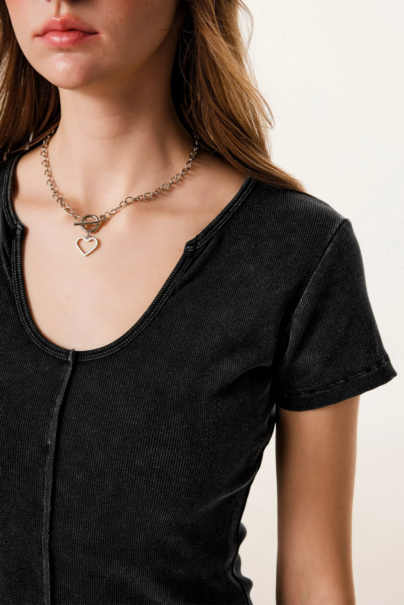 Person wearing a black shirt and gold necklace with heart pendants on a neutral background