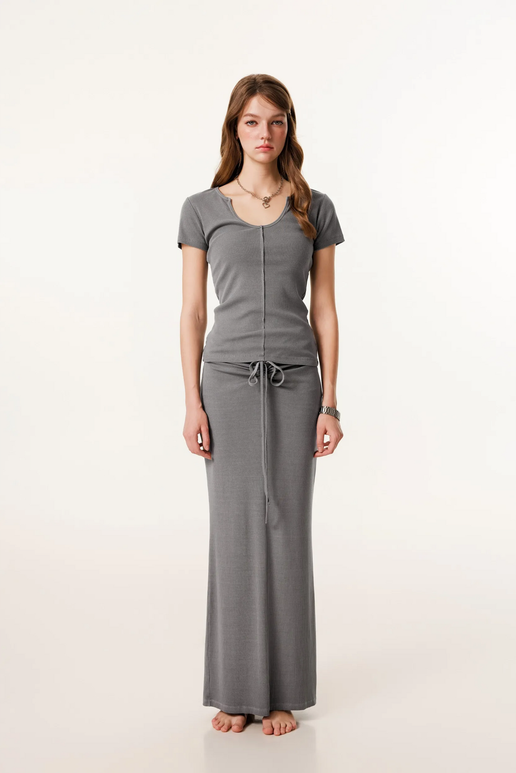Woman wearing a gray outfit with a top and long skirt on a white background