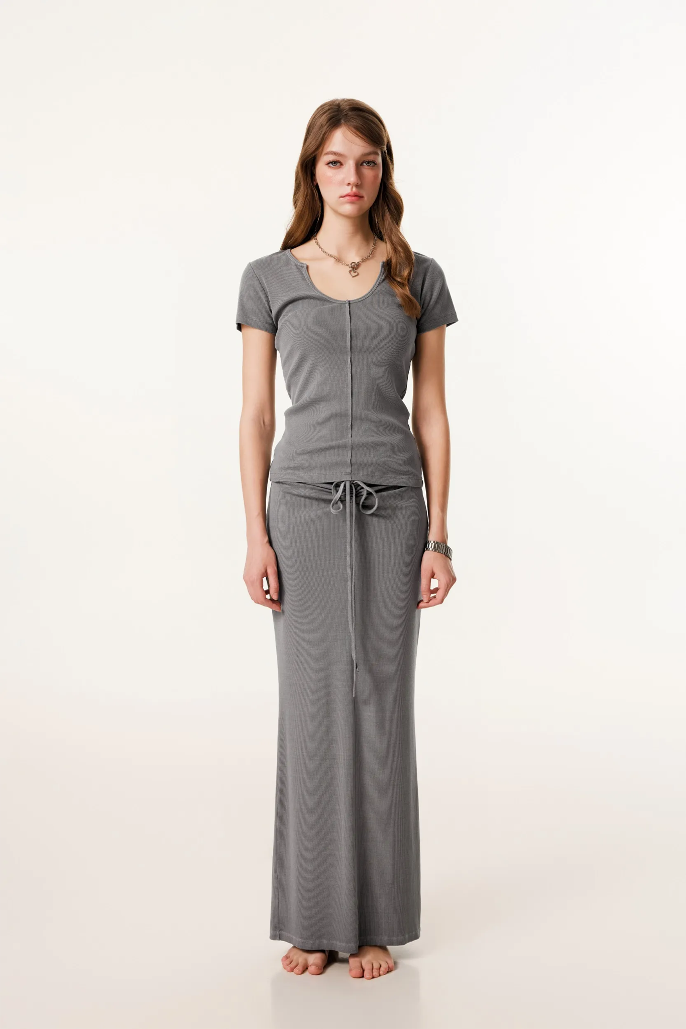 Woman wearing a gray outfit with a top and long skirt on a white background