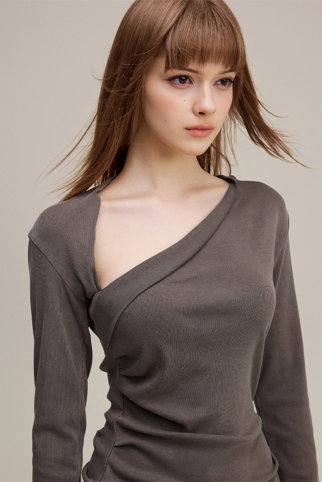 Woman wearing a brown long-sleeve top against a neutral background
