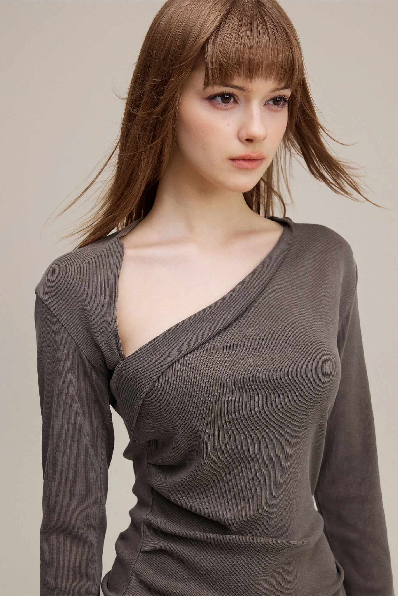 Woman wearing a brown long-sleeve top against a neutral background