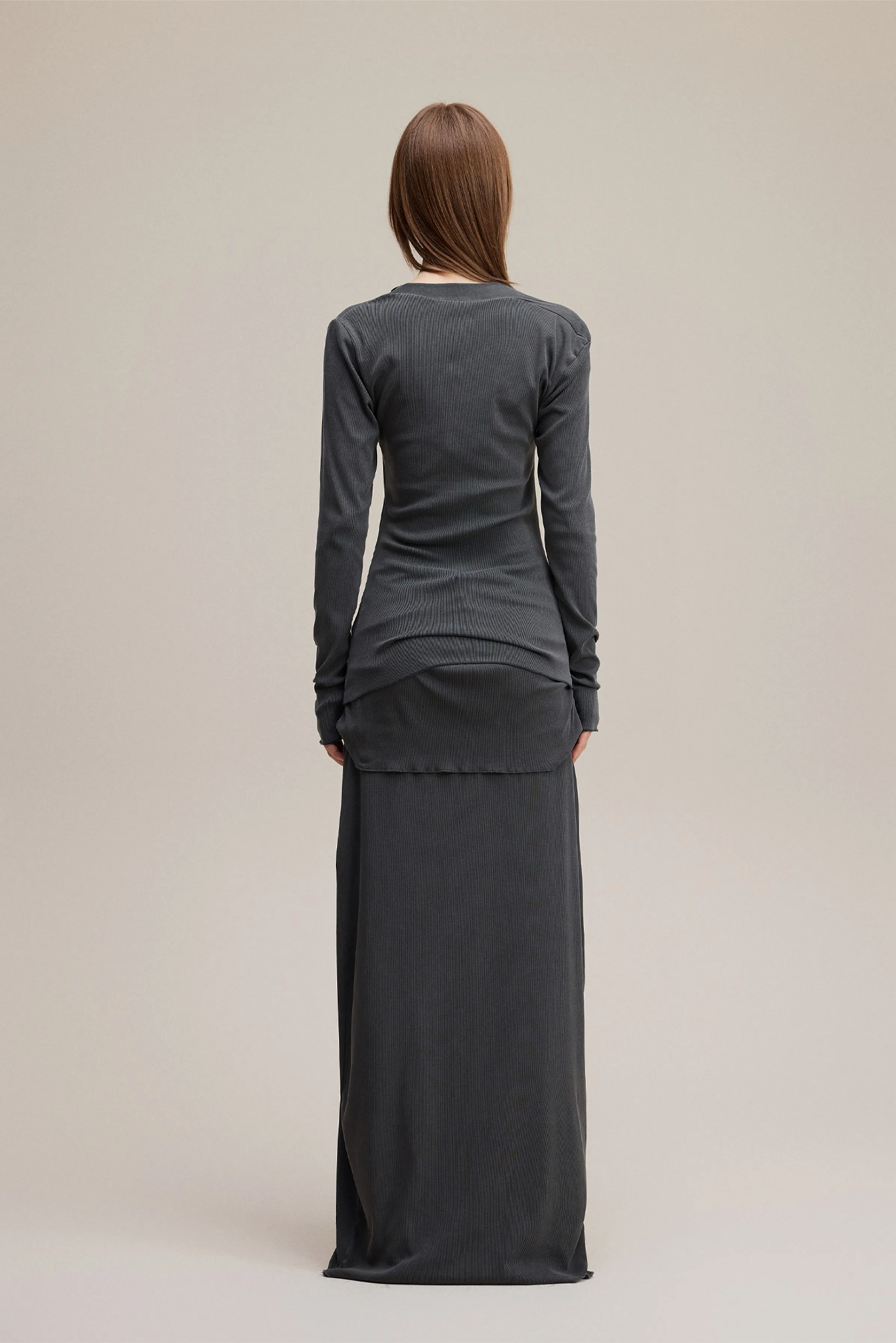 Person wearing a long dark gray dress on a beige background