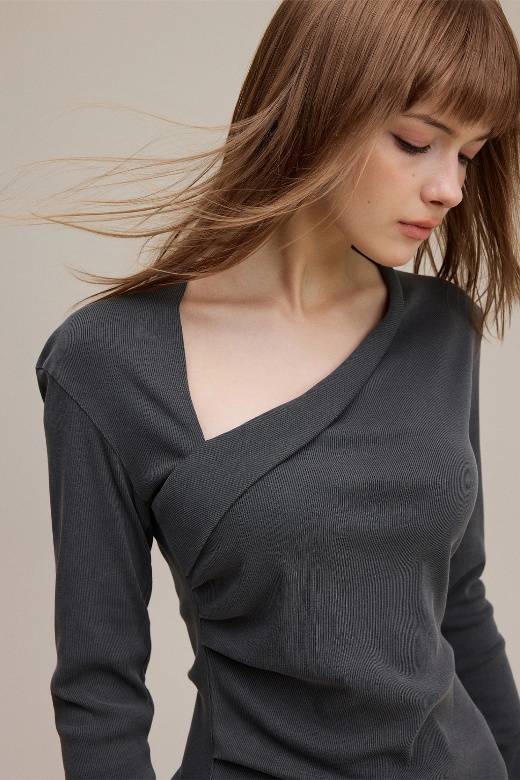 Woman wearing a dark gray long-sleeve top against a neutral background