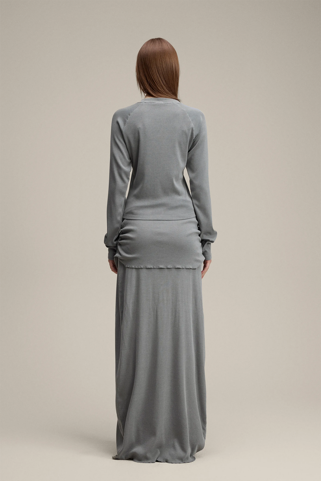 Woman wearing a gray long-sleeve top and long skirt set on a beige background