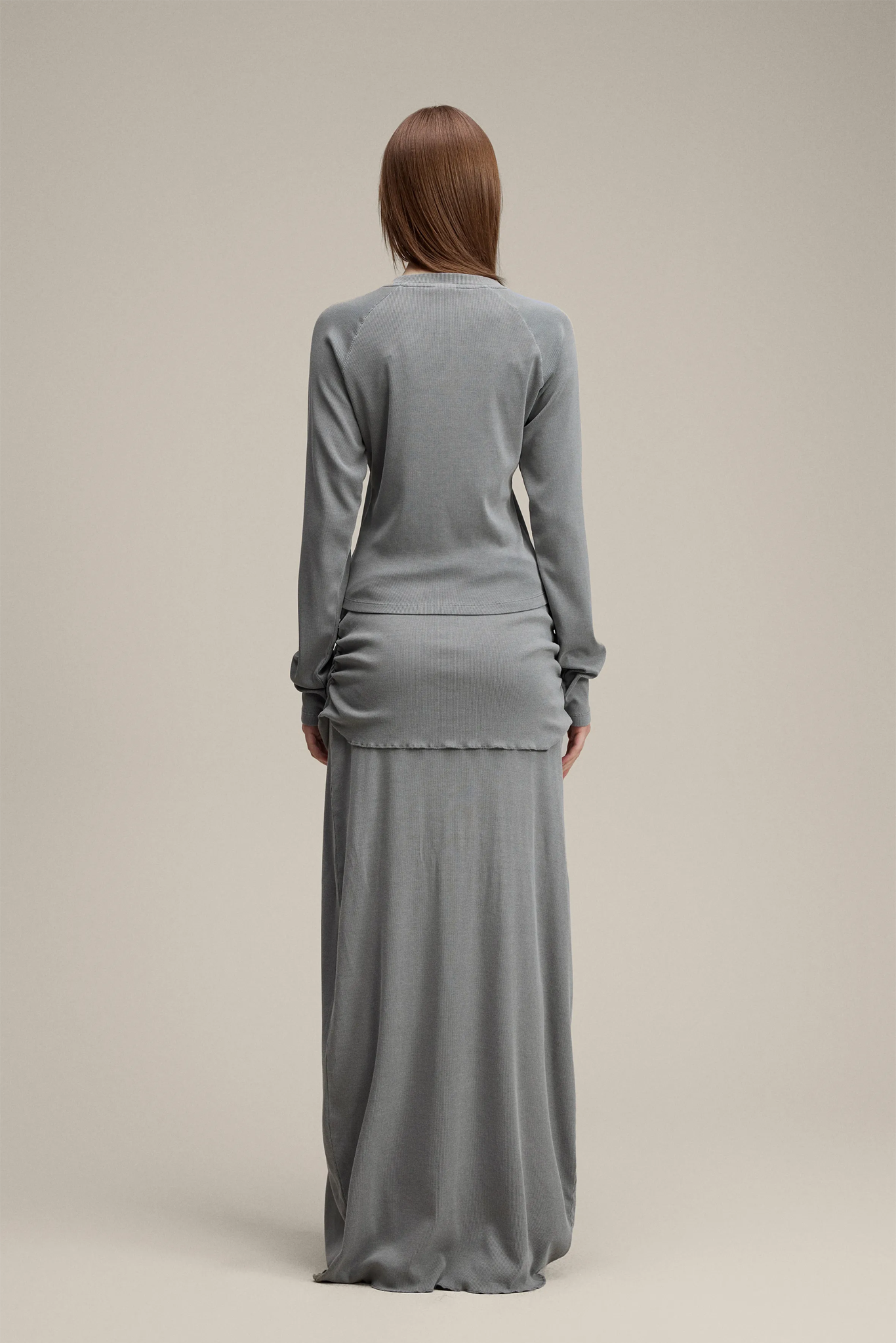 Woman wearing a gray long-sleeve top and long skirt set on a beige background
