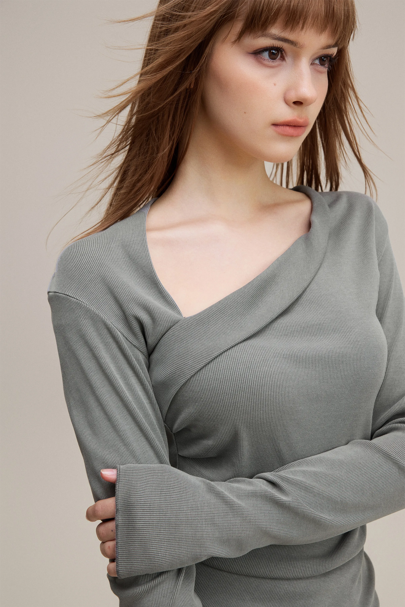Woman wearing a gray long-sleeve top against a neutral background