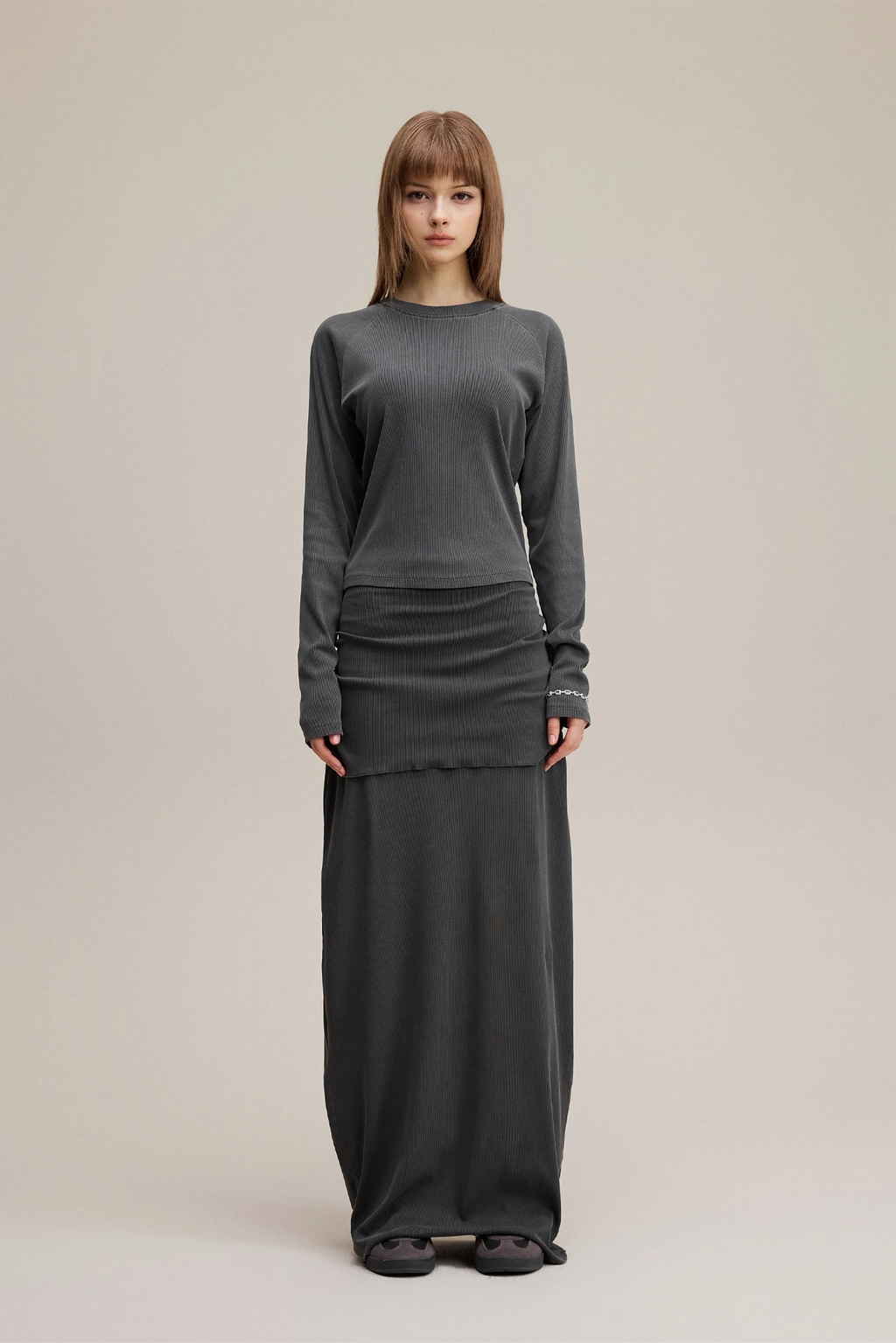 Person wearing a gray sweater and long dark skirt on a beige background