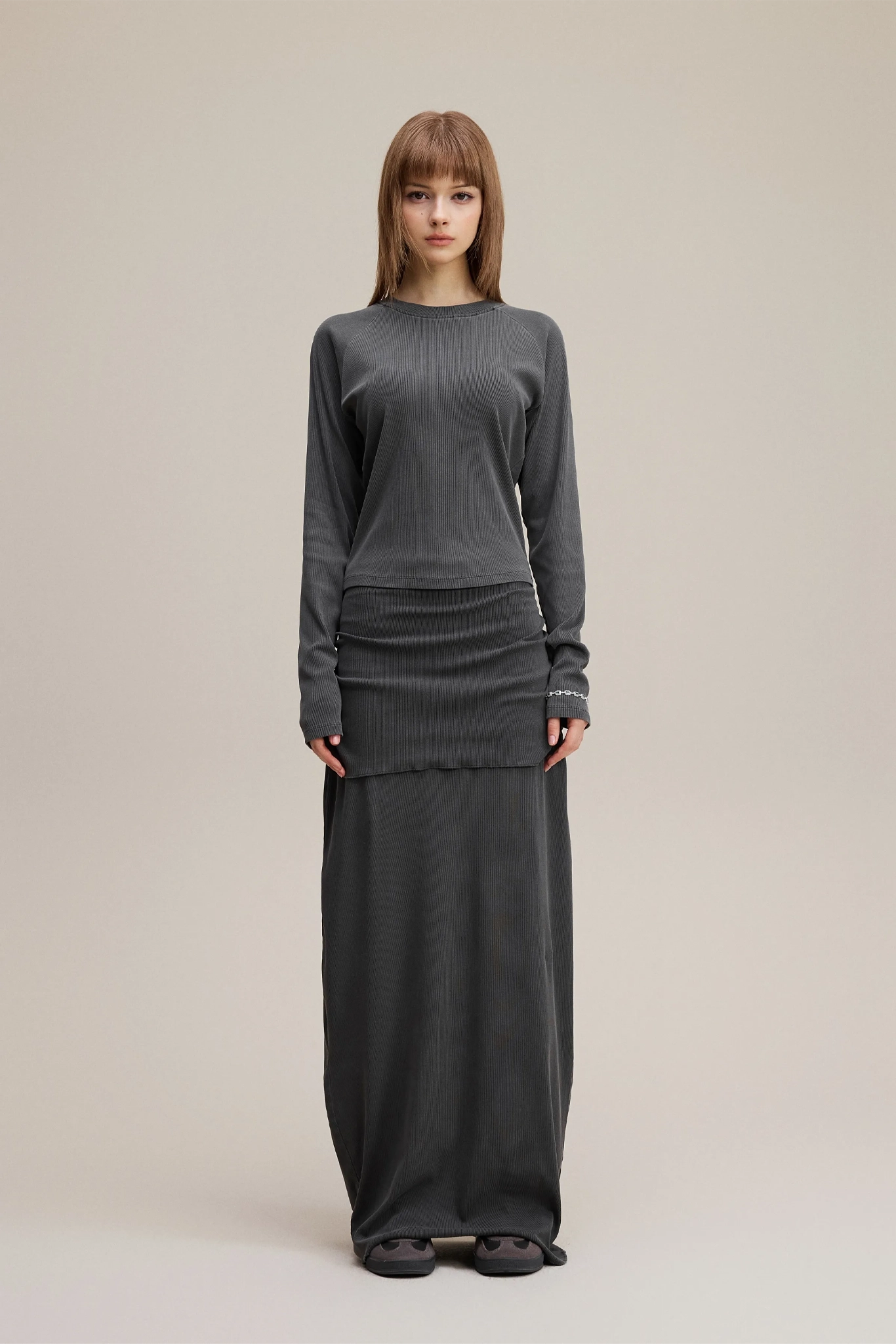 Person wearing a gray sweater and long dark skirt on a beige background