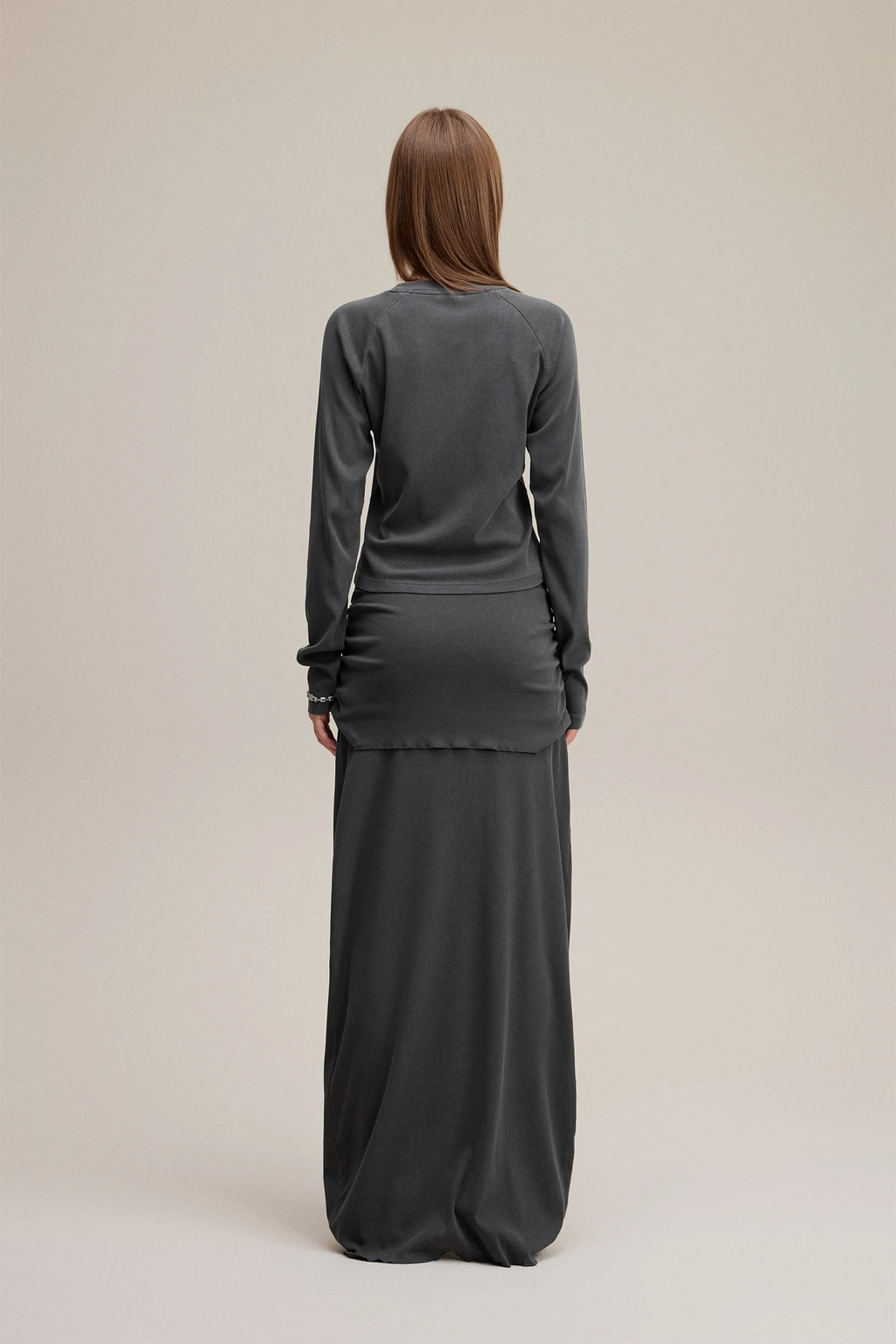 Person wearing a long dark gray dress with a matching top on a beige background