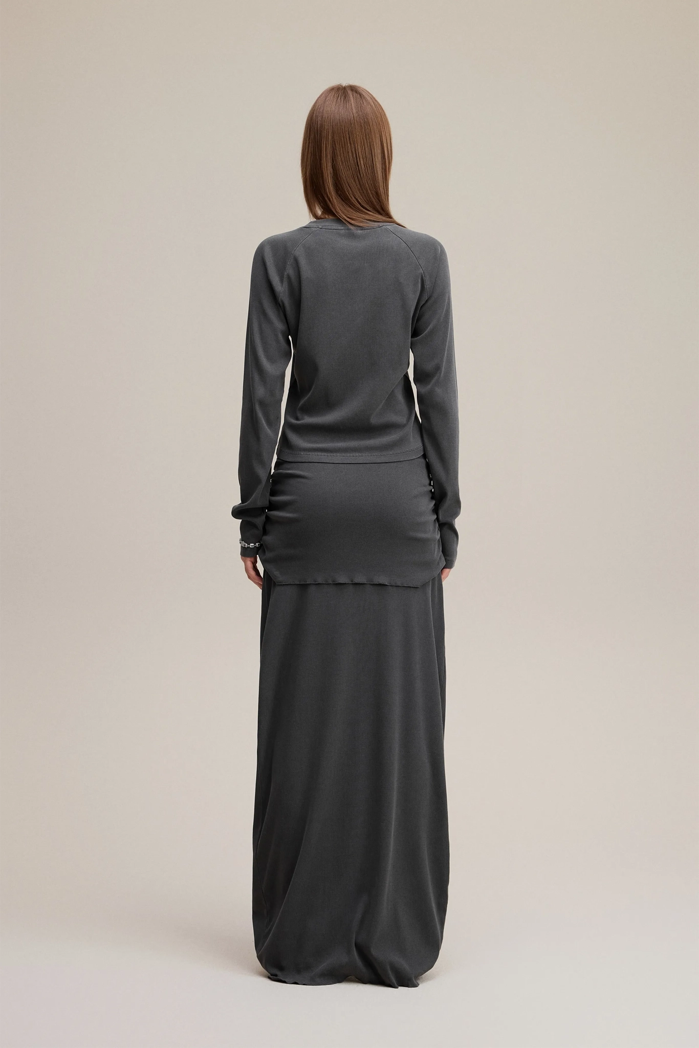 Person wearing a long dark gray dress with a matching top on a beige background