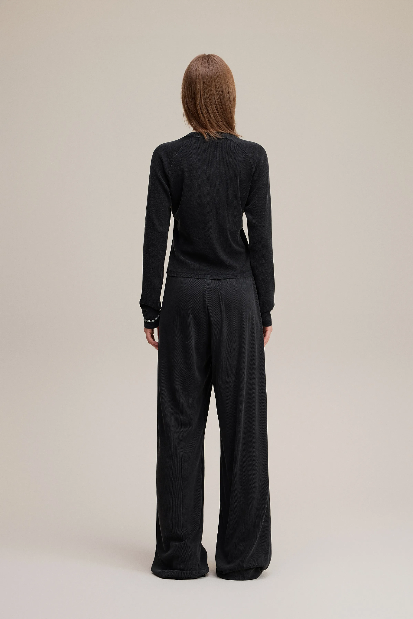 Person wearing a black outfit with wide-leg pants on a beige background