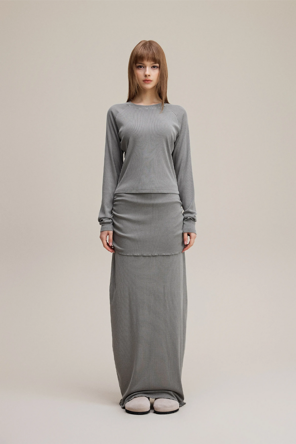 Woman wearing a gray long-sleeve top and skirt set on a beige background