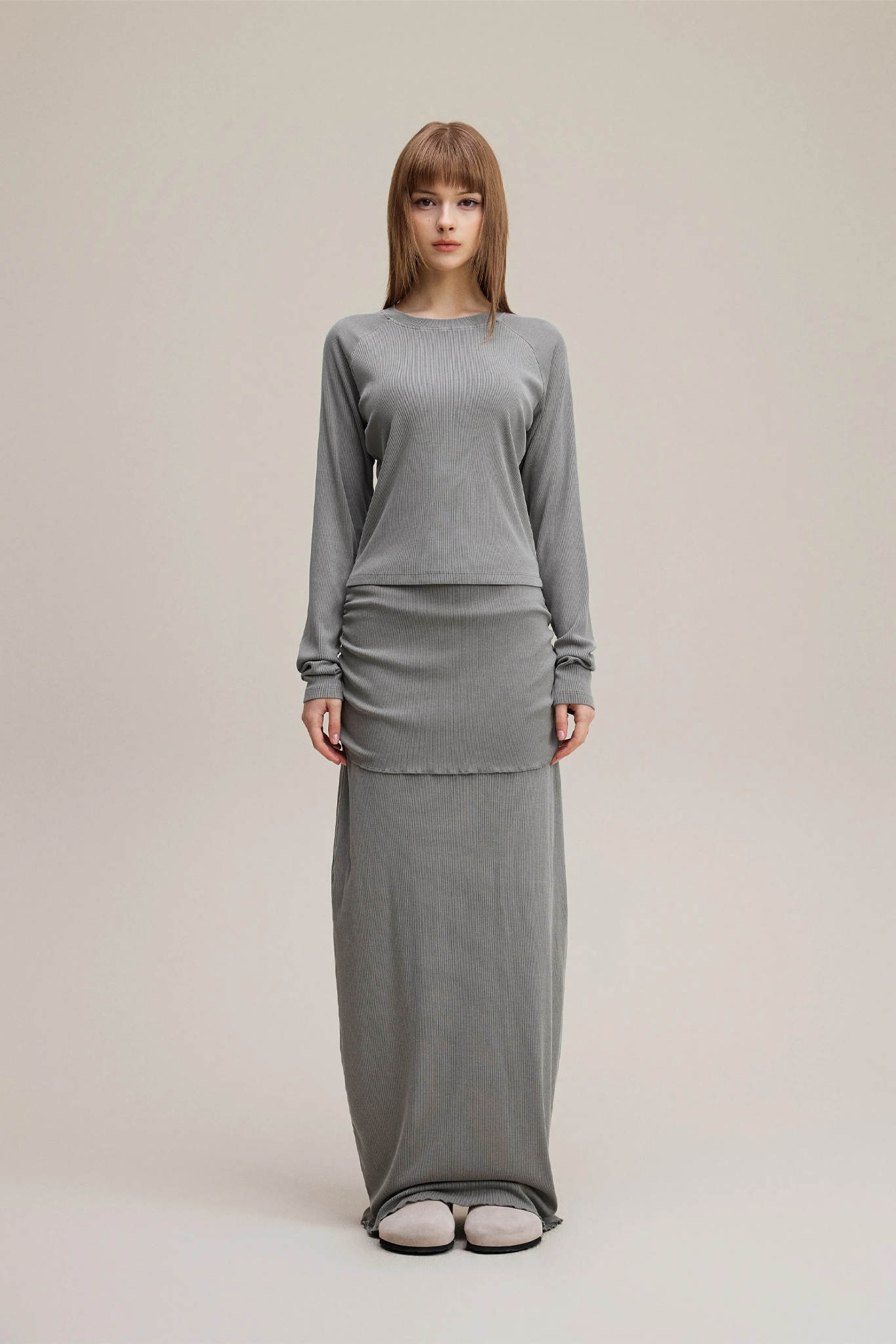Woman wearing a gray long-sleeve top and skirt set on a beige background