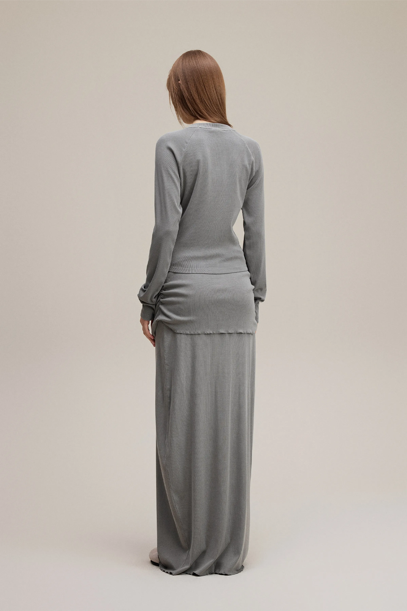 Woman wearing a gray long-sleeve top and skirt set on a plain background