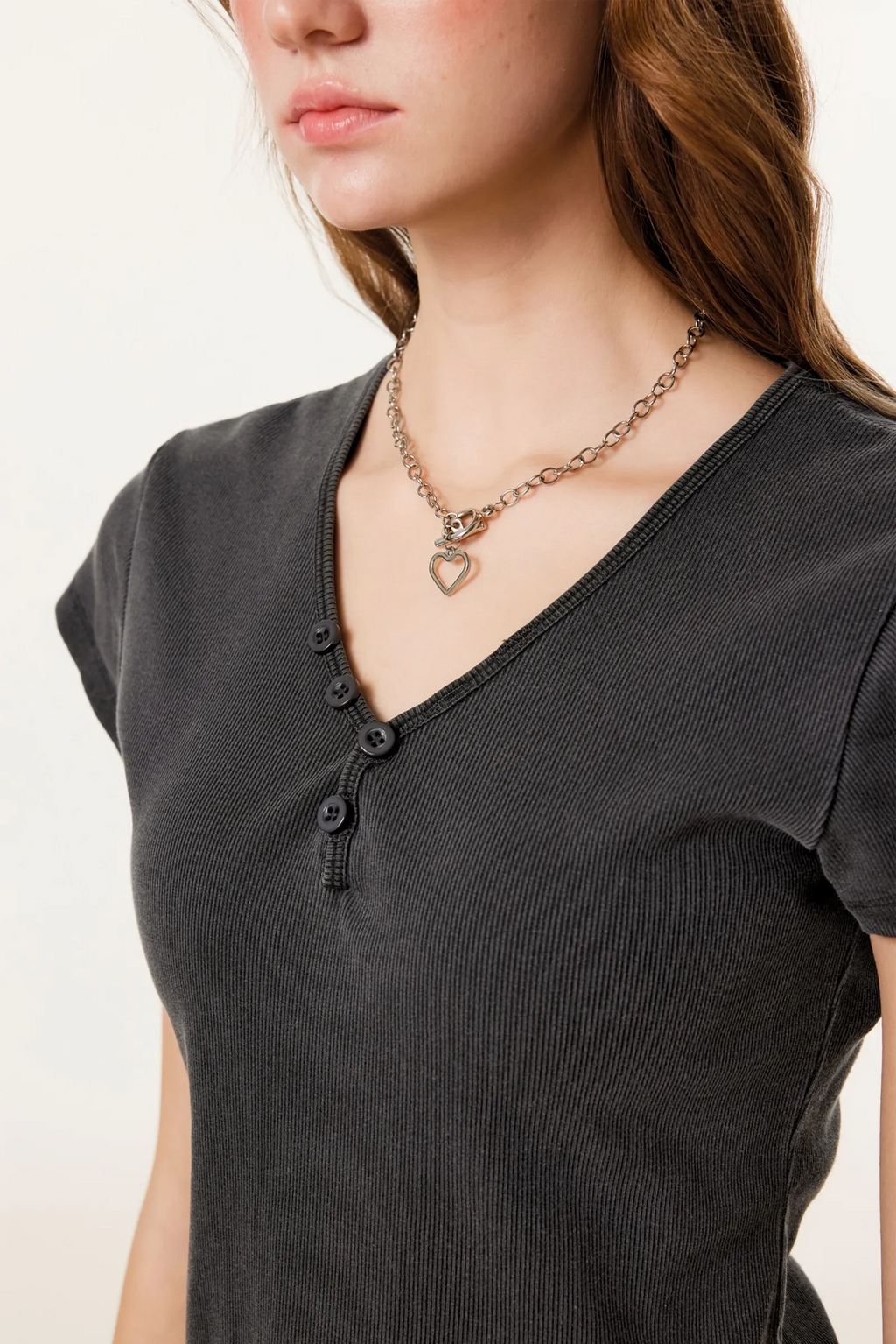 Person wearing a black shirt and a necklace with a heart pendant on a plain background