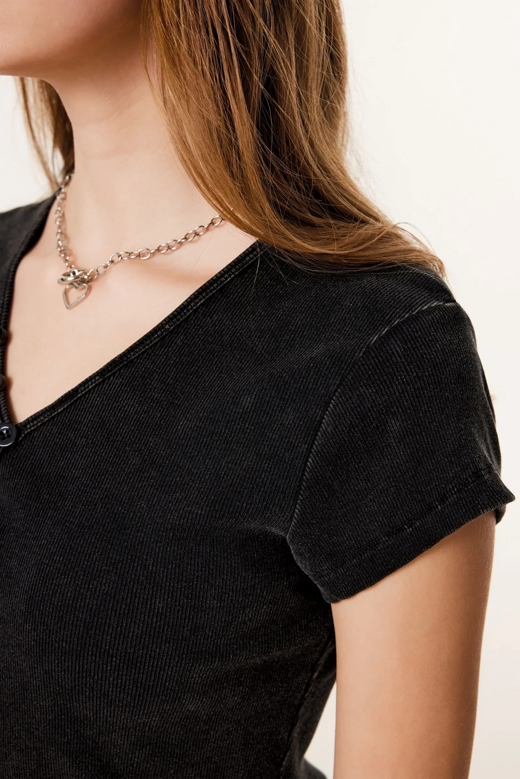 Person wearing a black top and a necklace with a heart pendant on a plain background