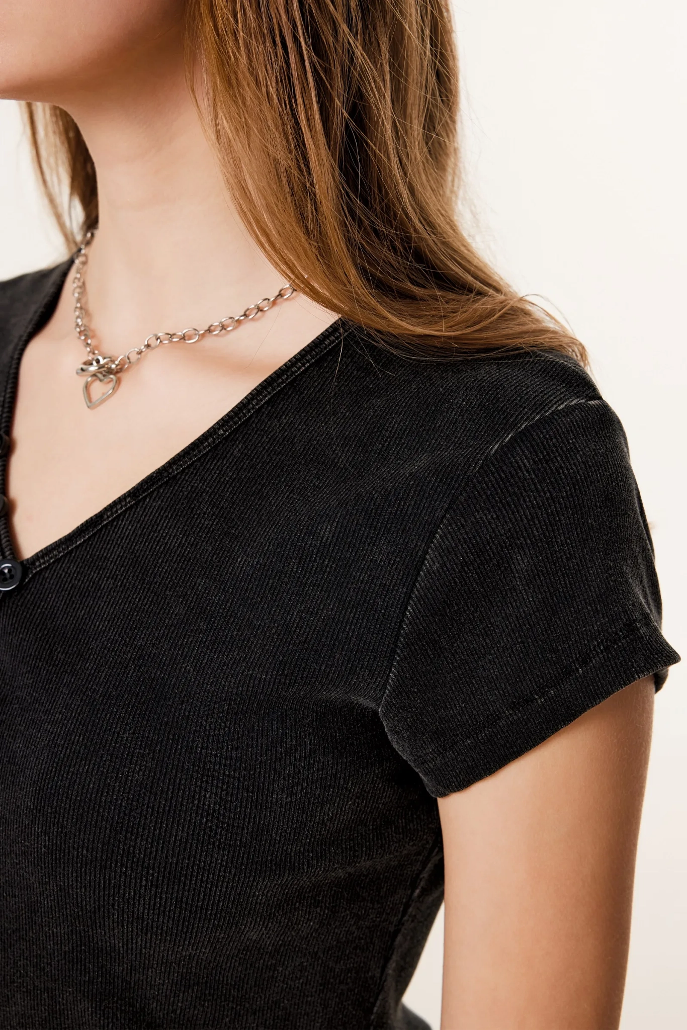 Person wearing a black top and a necklace with a heart pendant on a plain background