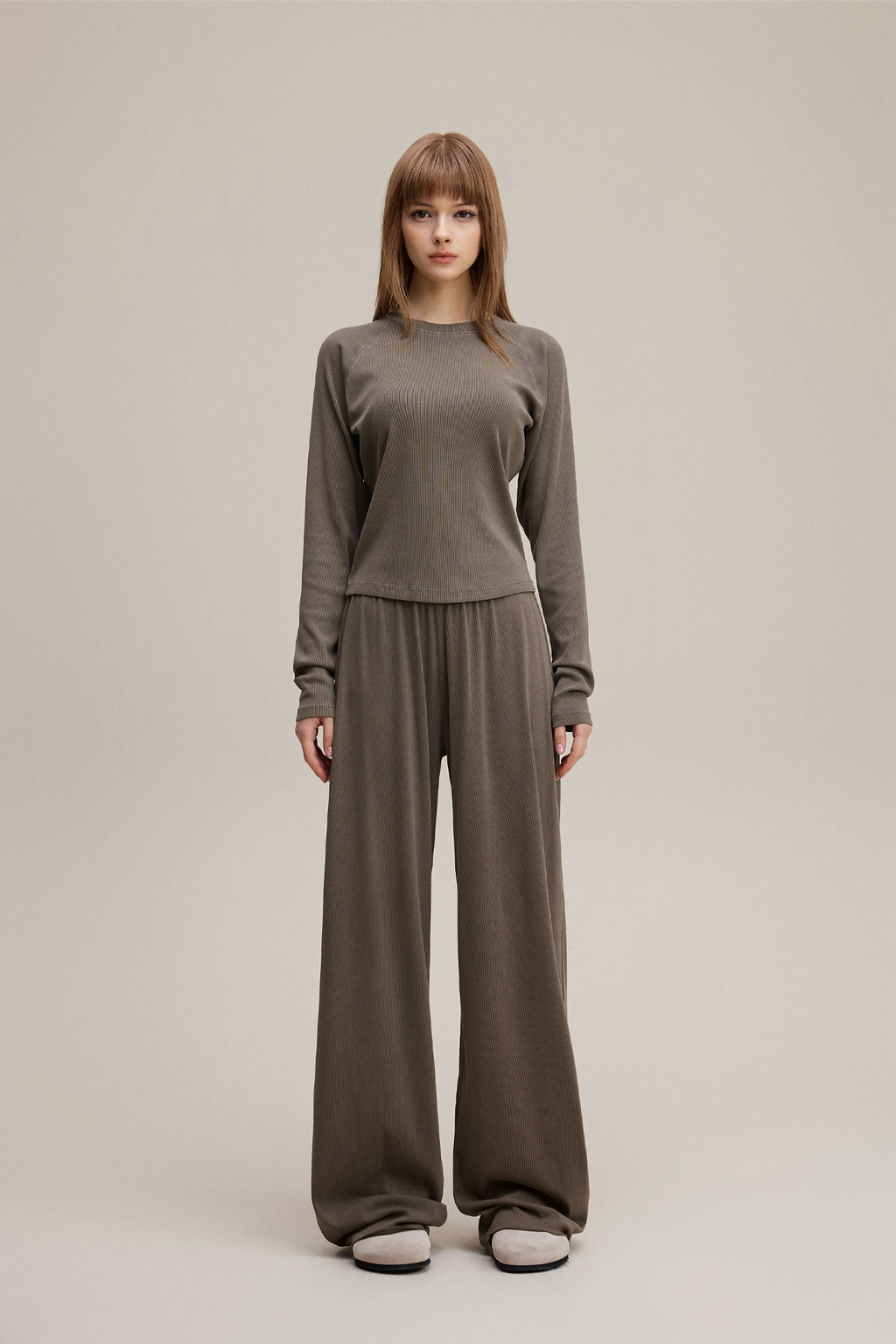 Woman wearing a gray sweater and brown pants on a beige background