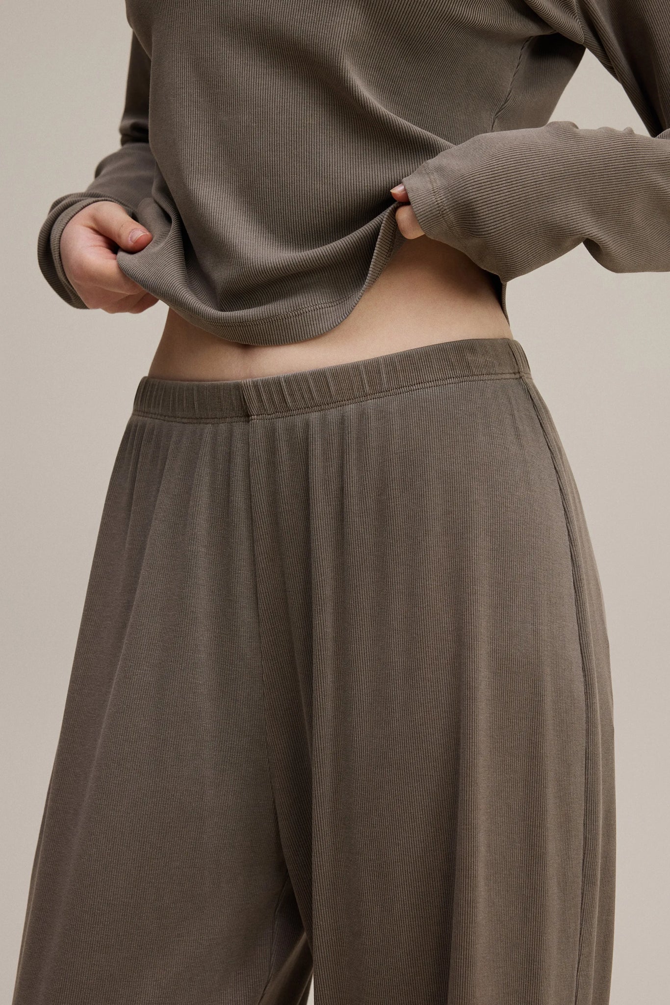 Person wearing a brown sweatshirt and pants on a beige background