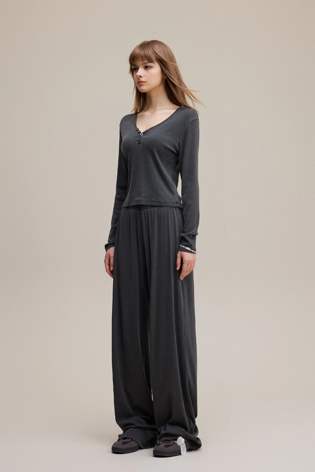 Woman wearing a dark gray long-sleeve top and wide-leg pants on a beige background