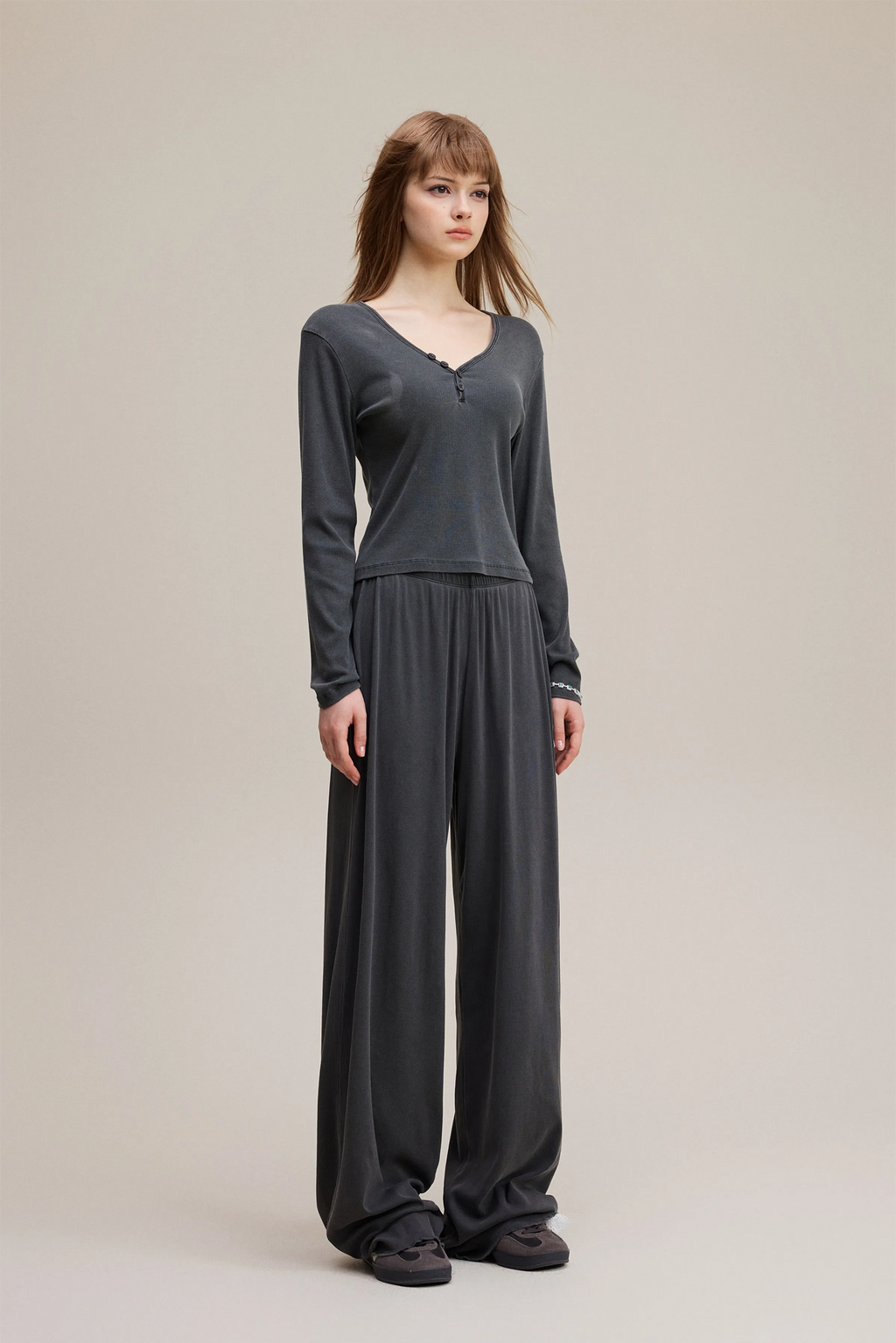 Woman wearing a long-sleeve gray top and wide-leg pants on a beige background