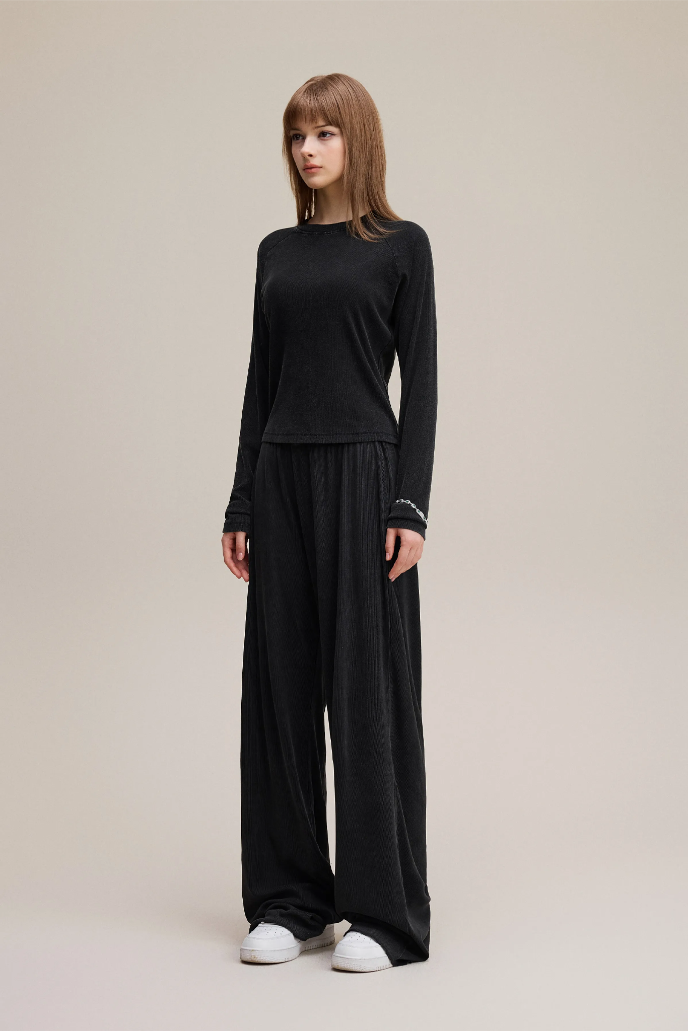 Woman wearing a black outfit with wide-leg pants on a beige background