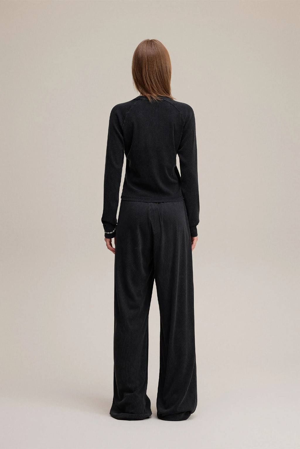 Person wearing a black outfit with wide-leg pants on a beige background