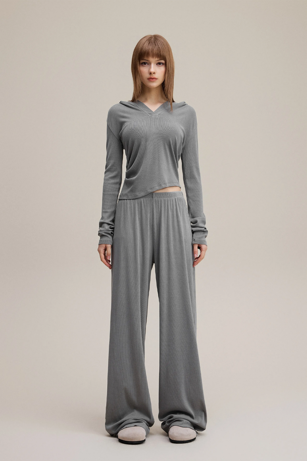 Woman wearing a gray long-sleeve top and wide-leg pants on a beige background